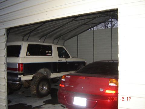 1988 Ford Bronco - Two vehicles, a lifted Ford Bronco and a red Dodge Stratus, are parked inside a metal garage.