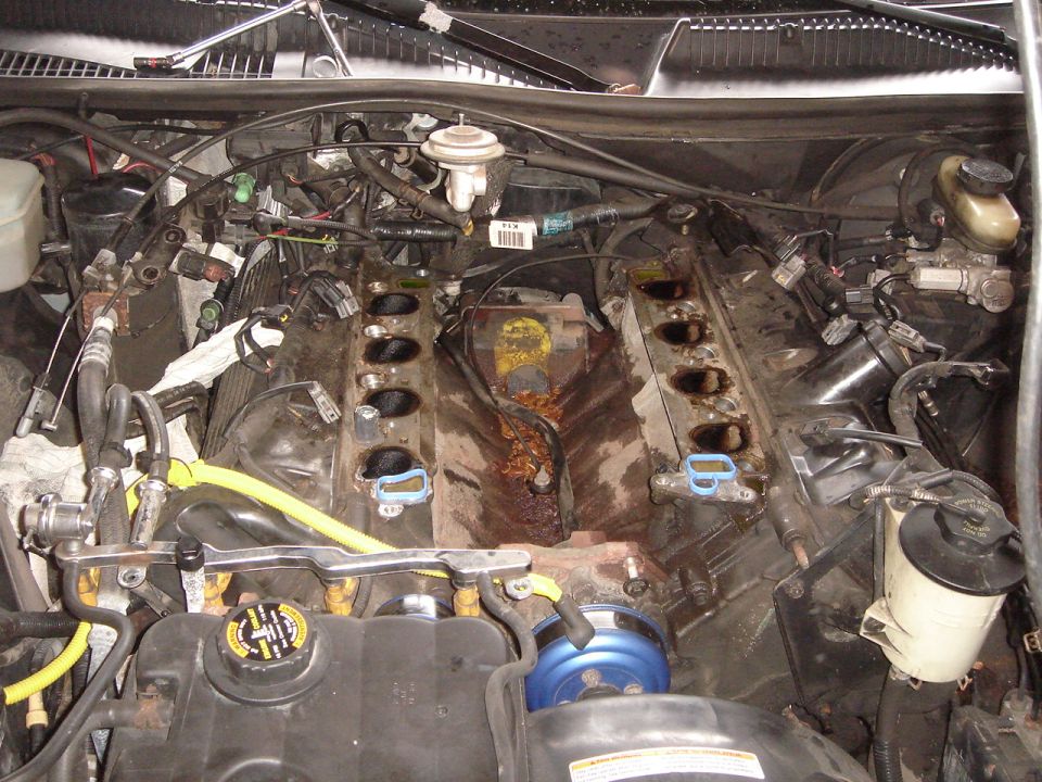 Engine bay with intake manifold off, showing the cylinder heads and fuel rails. Some rust and grime visible
