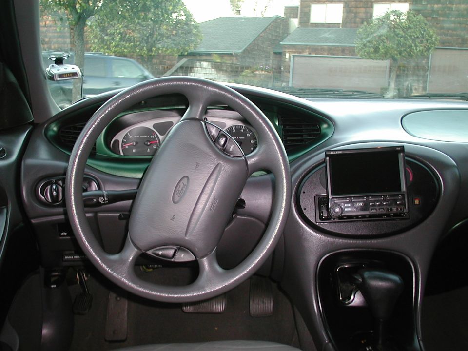 Gray Ford Taurus interior with steering wheel, aftermarket flip-out screen stereo, and radar detector
