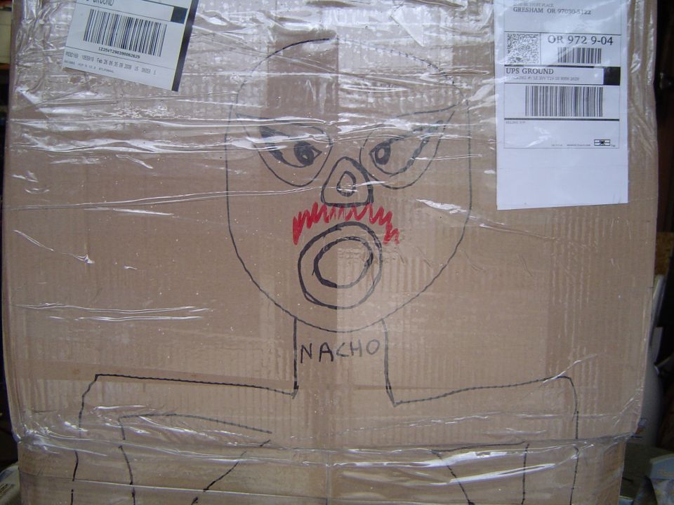 Cardboard shipping box with a marker drawing of a luchador labeled NACHO and UPS labels