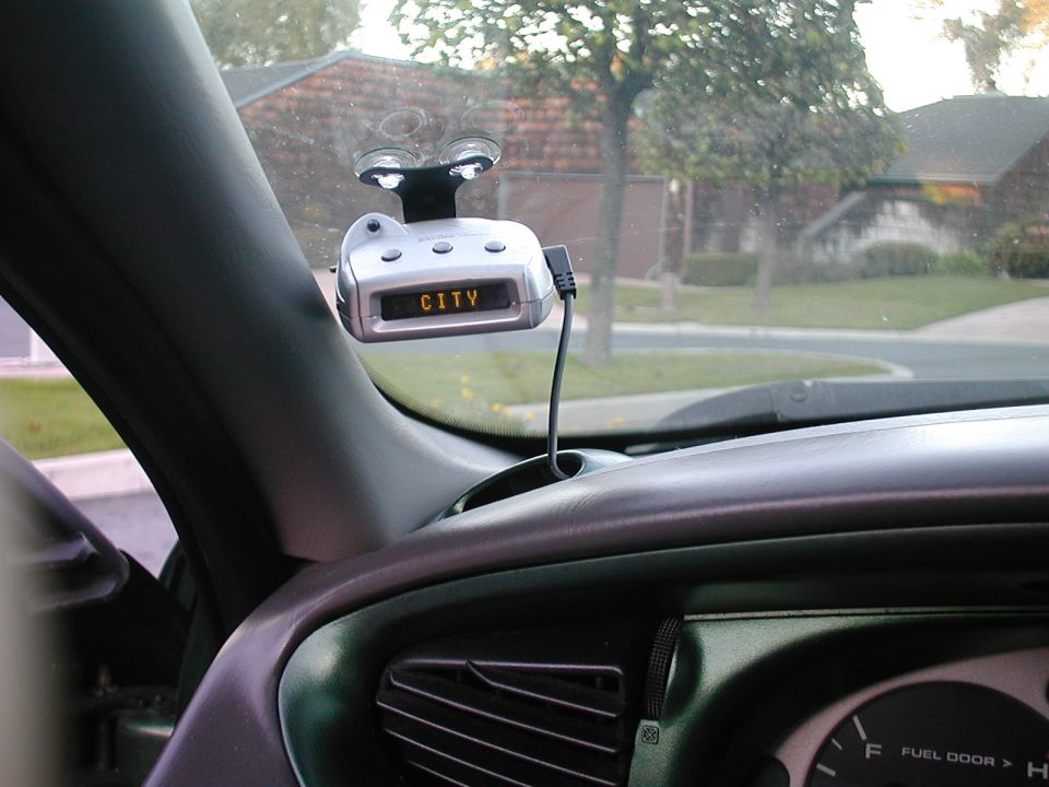 Silver radar detector displaying 'CITY' mounted on windshield above a gray car dashboard