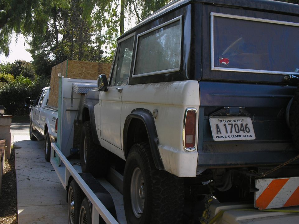 White classic Ford Bronco with dark top on a trailer towed by a white pickup, ND plate A 17046