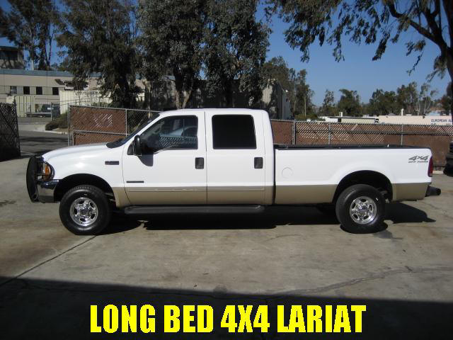 White and tan Ford Super Duty crew cab long bed 4x4 pickup, side view