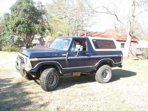 1978 Ford Bronco - A dark blue 1978 Ford Bronco with a white removable top sits parked on a grassy area.