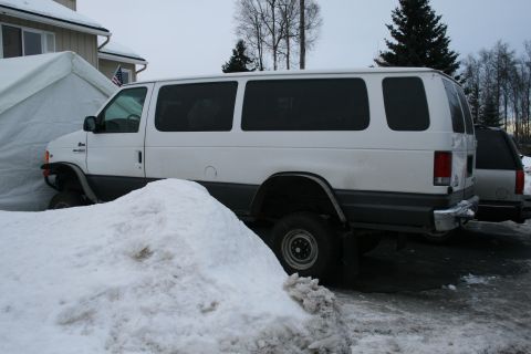 2003 Jeep TJ - A white van is parked in a snowy area next to a house and another vehicle.