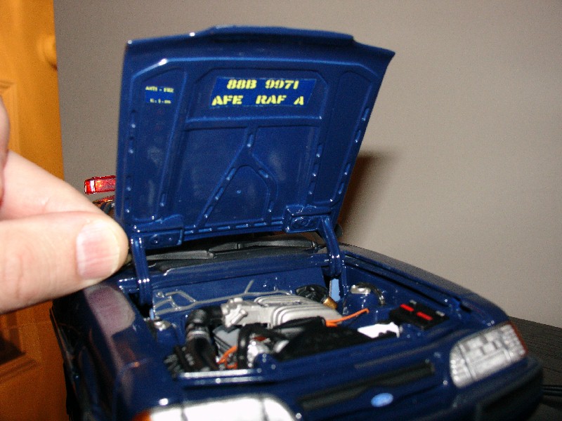 Dark blue scale model police sedan with hood open showing detailed miniature V8 engine