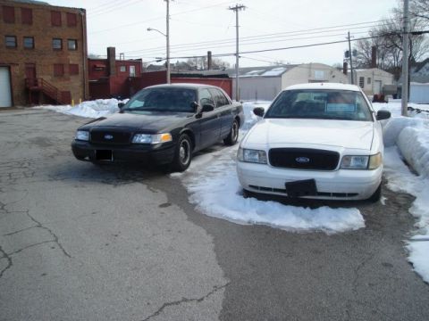 2000 Ford Crown Victoria - Two Ford Crown Victorias are parked in a lot with snow and ice around them.