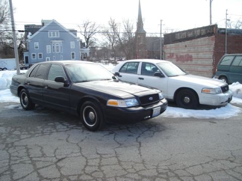 2000 Ford Crown Victoria - Two Ford Crown Victoria police cars are parked on a cracked asphalt lot with snow on the ground.