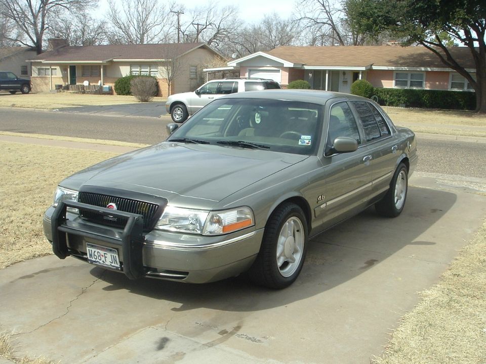 Green Mercury Grand Marquis sedan with black push bar, three-quarter front view in a driveway