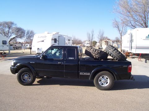 2003 Ford Ranger - A black 2003 Ford Ranger Edge pickup truck is parked outdoors, carrying two large off-road tires in its bed.