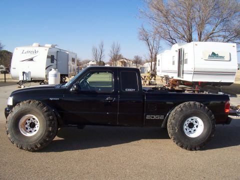 2003 Ford Ranger - Side view of a black 2003 Ford Ranger pickup truck modified with oversized tires and towing a trailer.