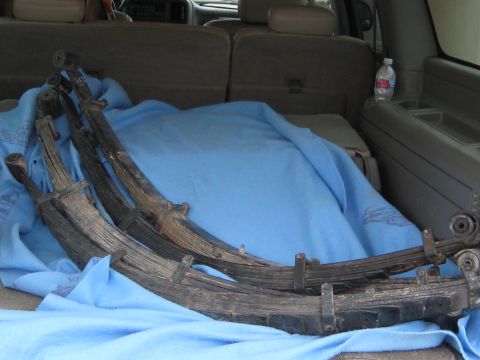 1996 Ford Bronco - Several used leaf springs are laid out on a blue blanket inside the cargo area of a vehicle.
