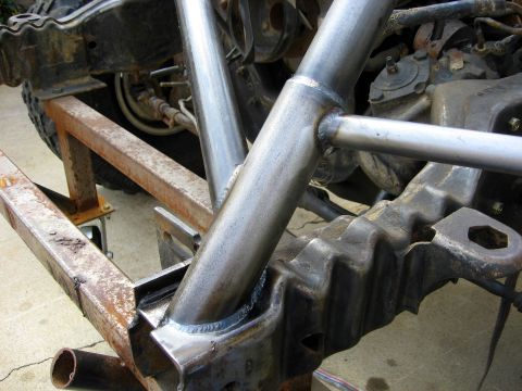 1995 Ford Bronco - Close-up view of a custom roll cage being fabricated and welded onto a vehicle's frame, with suspension parts visible.