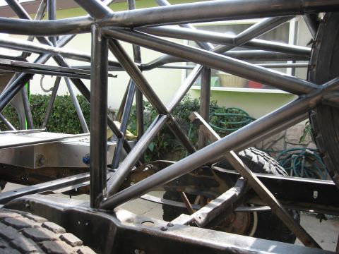 1995 Ford Bronco - The intricate metal framework of a custom vehicle chassis is visible, with parts of the suspension and tires in view.