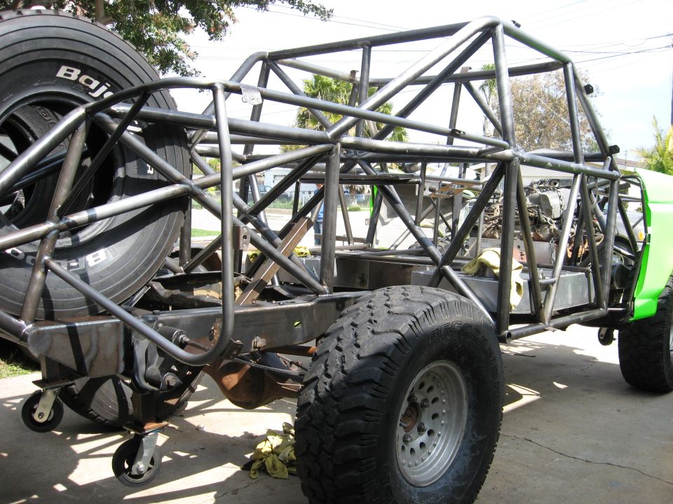 Off-road race truck chassis with roll cage, spare tire, and large off-road tires. Green body panel visible at front right