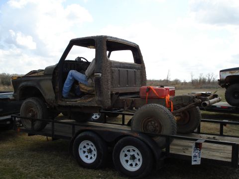 2008 International School Bus - A heavily weathered truck chassis is transported on a trailer, with a person occupying the driver's seat.