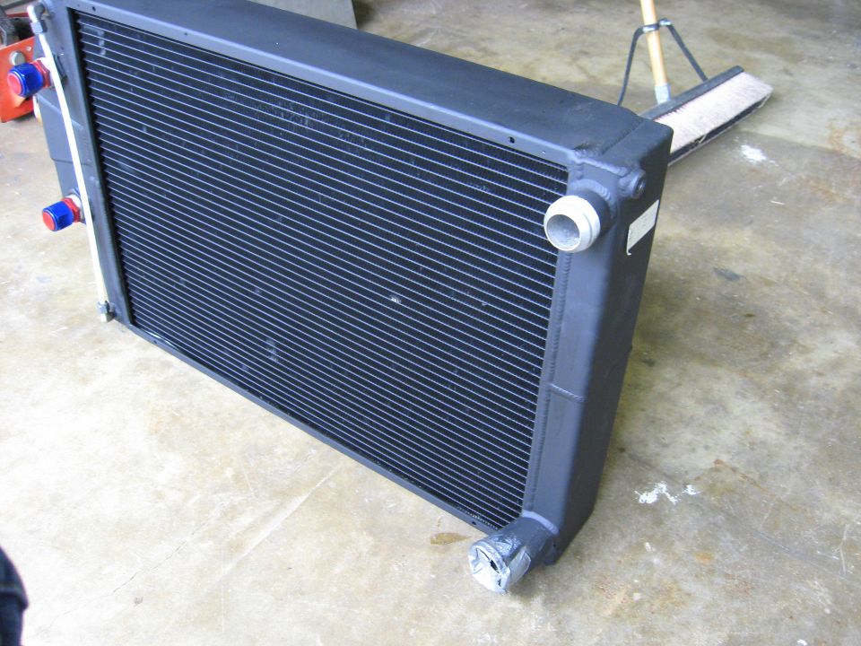 Black radiator with blue and red fittings on the left side, viewed from a 3/4 front angle