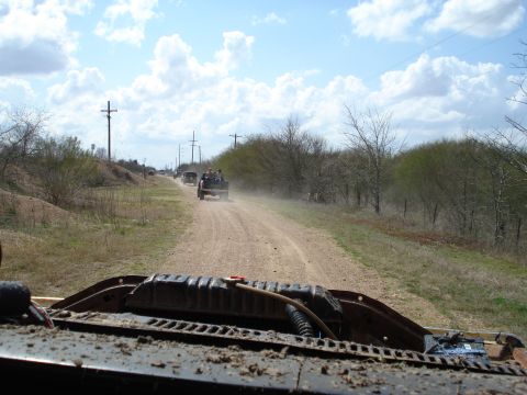 2008 International School Bus - A convoy of vehicles travels down a dirt road, kicking up dust under a cloudy sky.