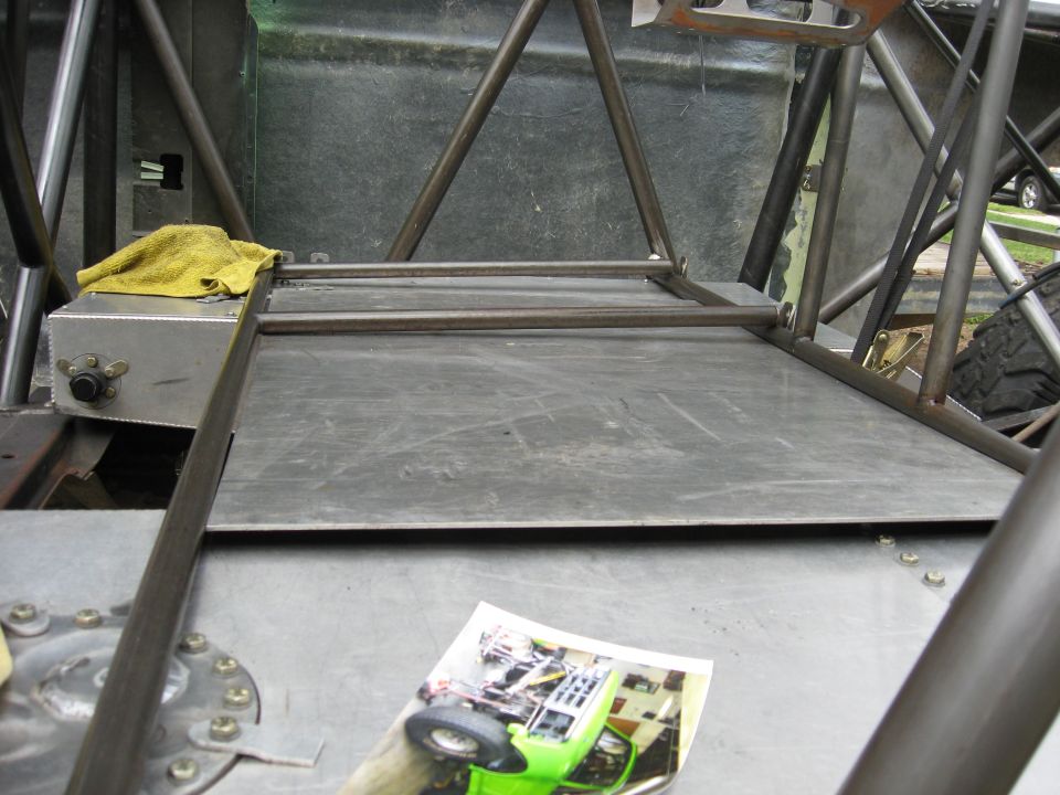 Interior of a custom off-road vehicle with a yellow rag on a metal box, and a photo of a green buggy on the floor