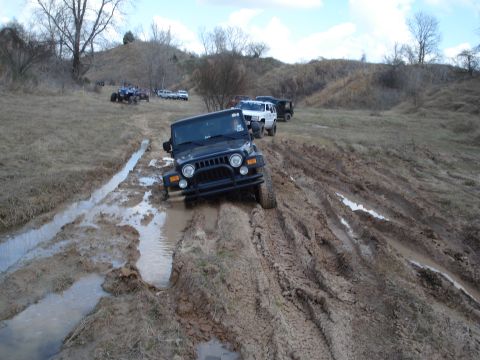 2008 International School Bus - Several off-road vehicles traverse a challenging muddy terrain, with a black Jeep Wrangler prominently featured in the foreground.