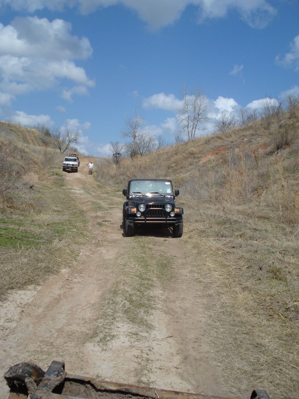 Black Jeep Wrangler TJ driving up a dirt hill with another Jeep behind it