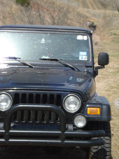 2008 International School Bus - A dark blue Jeep Wrangler is shown from the front, with a bull bar and dusty windshield, while an ATV is visible in the background on a hil…