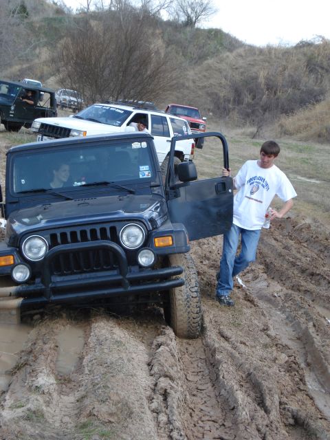2008 International School Bus - Several off-road vehicles navigate a muddy terrain, with one Jeep Wrangler prominently stuck.