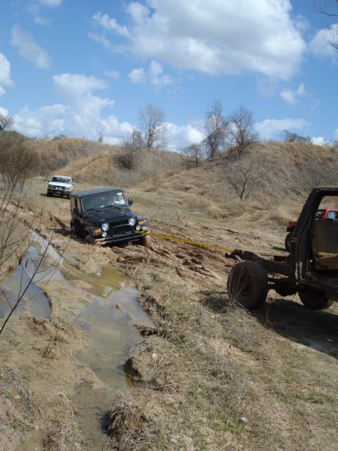 2008 International School Bus - Multiple off-road vehicles navigate a muddy trail with one Jeep requiring assistance from a tow strap.