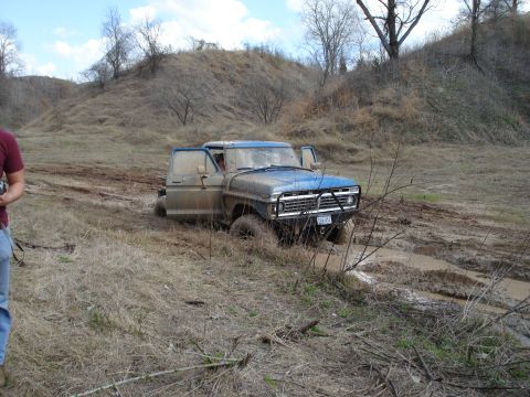 2008 International School Bus - A blue pickup truck is stuck in a muddy ditch, with its doors open.