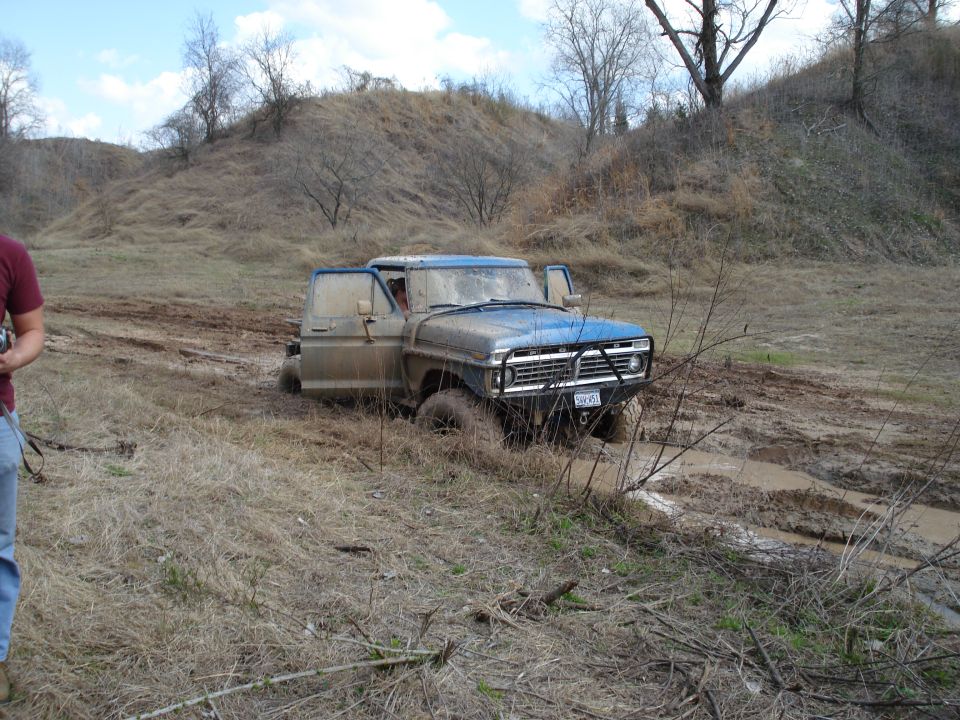 Blue pickup truck stuck in mud, front view. License plate reads '104 V51'