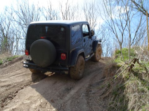2008 International School Bus - A black Jeep Wrangler navigates a muddy, off-road trail, kicking up dirt as it ascends the incline.