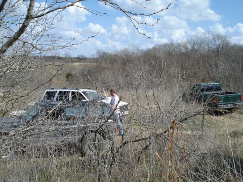 2008 International School Bus - Two pickup trucks are parked in a dry, brush-filled field under a partly cloudy sky.