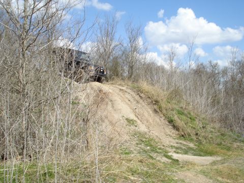 2008 International School Bus - A dark-colored SUV navigates a steep, sandy incline surrounded by sparse vegetation under a partly cloudy sky.