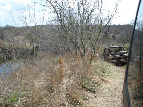 2008 International School Bus - An old pickup truck navigates a rough, off-road path near a body of water.