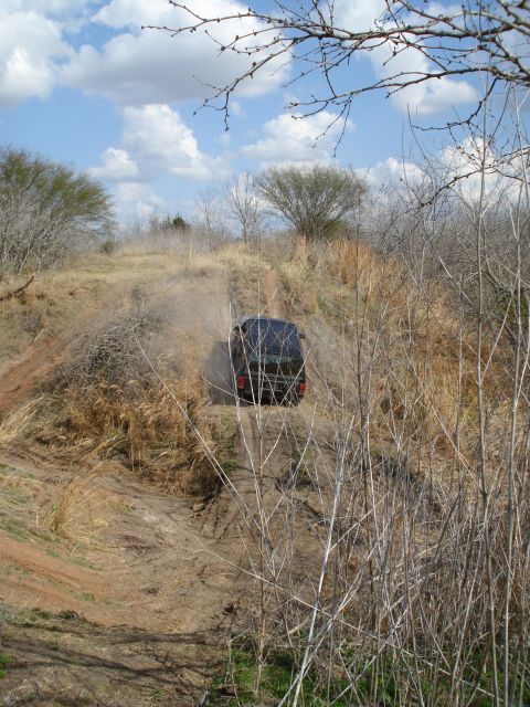 2008 International School Bus - A vehicle navigates a dusty, off-road trail surrounded by dry vegetation under a cloudy sky.