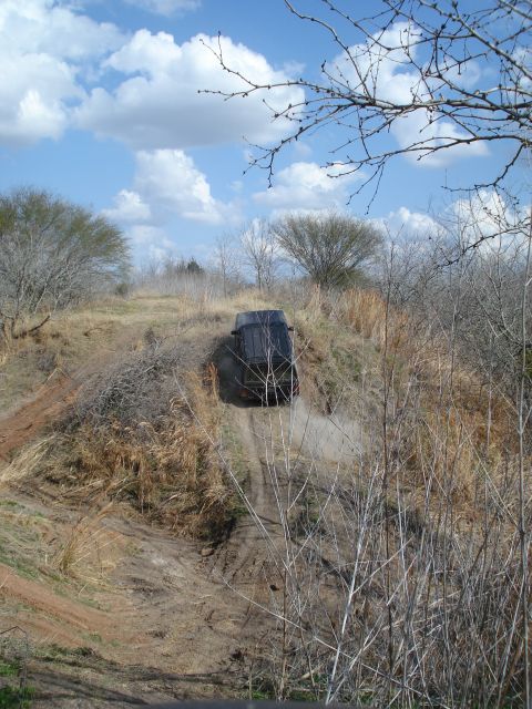 2008 International School Bus - A dark SUV navigates an off-road trail, kicking up dust as it ascends a steep, dry embankment.
