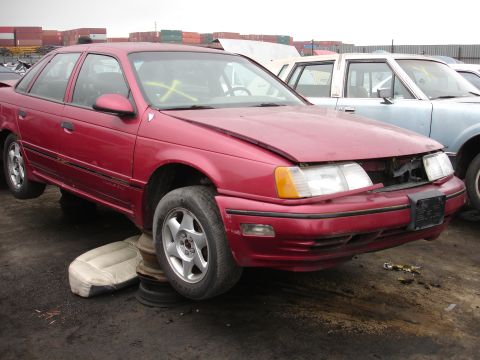 1993 Ford Taurus - Junkyard scene with a damaged red sedan and another vehicle in the background.