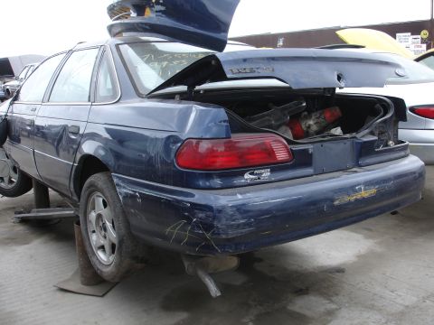 1993 Ford Taurus - The rear of a blue 1993 Ford Taurus sedan is shown with its trunk open, revealing contents and damage to the bumper.