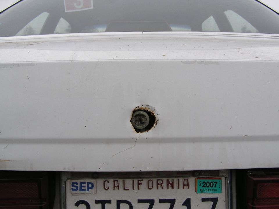 White car trunk lid with rusty damaged lock cylinder above a California license plate