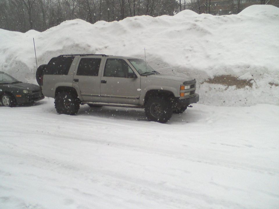 Silver Chevrolet Tahoe with aftermarket wheels parked in snow next to a dark sedan