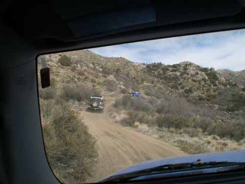 2007 Toyota FJ Cruiser - Two SUVs navigate a winding dirt road through a rocky, arid landscape under a cloudy sky.
