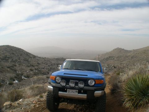 2007 Toyota FJ Cruiser - A blue Toyota FJ Cruiser navigates a dusty mountain trail under a hazy sky.