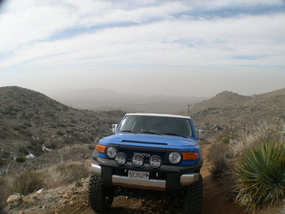 Blue Toyota FJ Cruiser with white roof and aftermarket lights on a dusty mountain trail