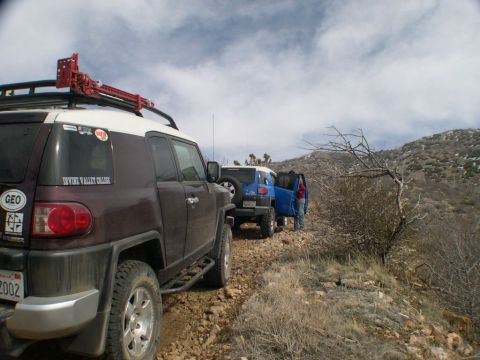 2007 Toyota FJ Cruiser - Two Toyota FJ Cruisers navigate a rocky trail, one equipped with a high-lift jack on its roof rack.
