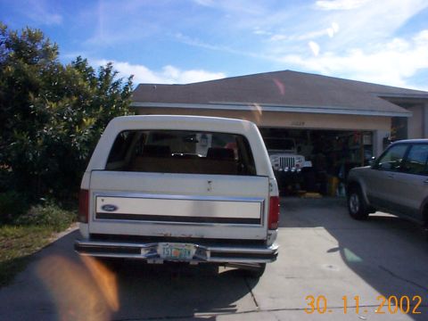 1985 Ford Bronco - The rear of a Ford Bronco is visible, parked in front of a garage with other vehicles.