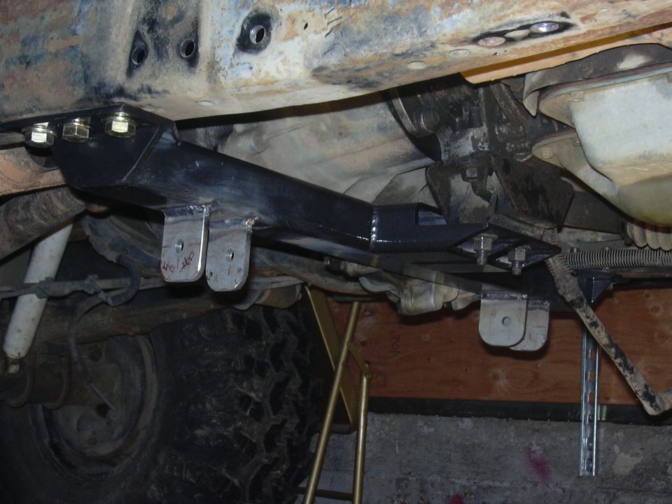 Aftermarket crossmember bolted to vehicle frame, showing suspension components and tire