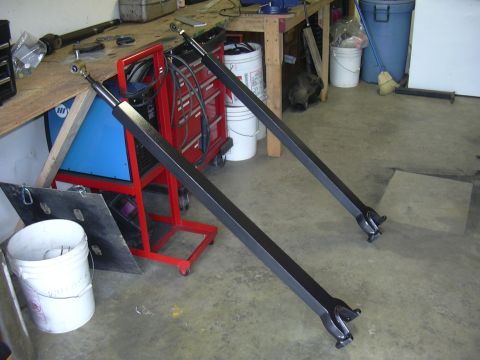 1991 Ford Bronco - Two black metal radius arms are visible in a workshop setting, resting on a concrete floor.