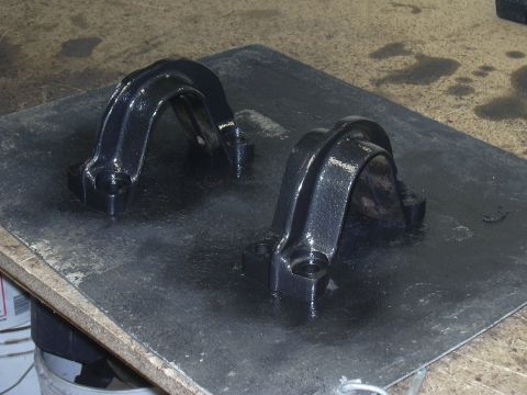 1991 Ford Bronco - Two freshly painted suspension brackets sit on a protective mat, ready for installation.