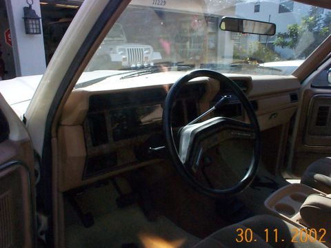 1985 Ford Bronco - The interior of an older SUV, likely from the 1980s, is shown. A Jeep is visible through the windshield.
