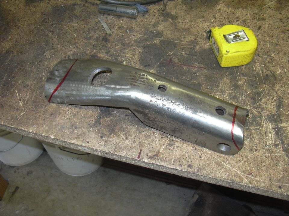 Metal automotive part with circular holes and red cut lines on a workbench next to a yellow tape measure